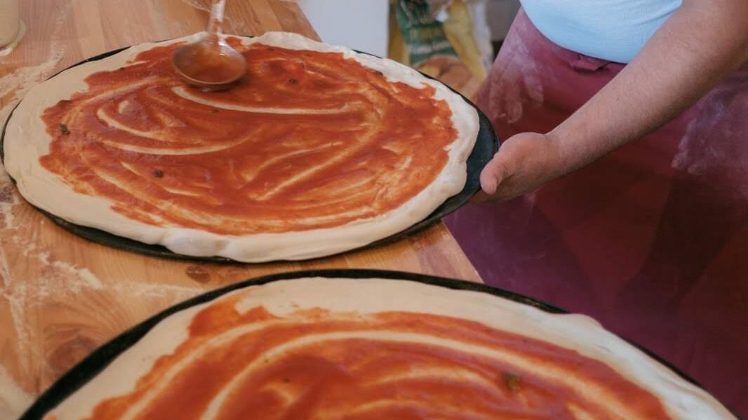Pizzaböden werden mit Tomatensoße bestrichen